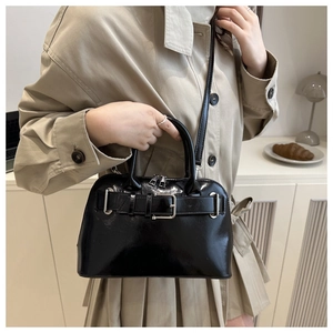 Detail of glossy black shell bag featuring a large silver metal buckle and belt decor