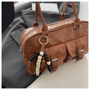 Detail of a brown leather Boston bag with double flap pockets and wood bead charm
