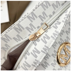 Detailed macro view of gold-tone M-logo hardware and black monogram on white leather tote