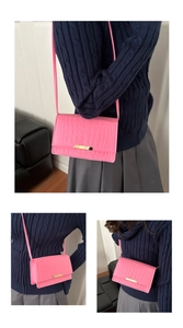 Detail of bright pink crocodile embossed leather crossbody bag with gold metal trim