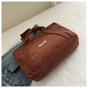 Close-up of brown corduroy tote bag with wide strap and white fashion woven label