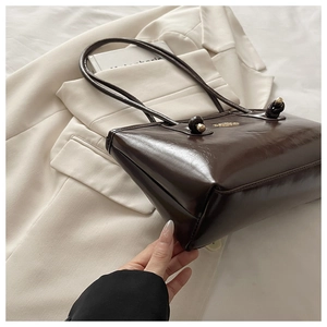 Detail of a dark brown glossy leather tote bag with gold metal plate on a white blazer