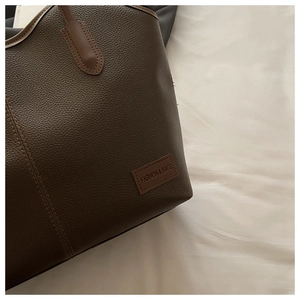 Detail of dark brown pebble leather tote bag featuring cream contrast stitching