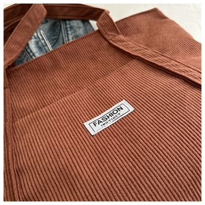 Detail of rust brown corduroy tote bag showing the fabric texture and fashion label