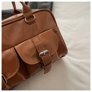 Detail of glossy brown faux leather handbag showing metal buckles and front pockets texture