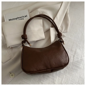 Detail of a dark brown half-moon hobo bag with a cylindrical strap and golden metal links