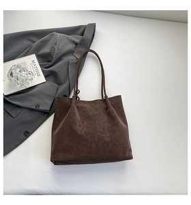 Flat lay of a large dark brown suede tote bag next to a grey blazer and art book