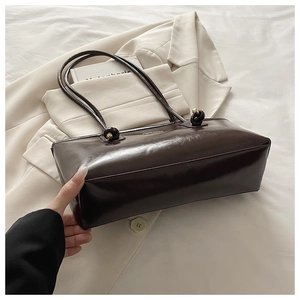 Detail of dark brown leather shoulder bag with knot strap on a beige blazer