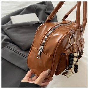 Close-up of brown glossy PU tote bag featuring silver zippers and beaded charm detail