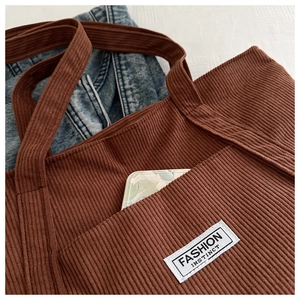 Detail view of brown corduroy tote bag featuring an front pocket and fashion label