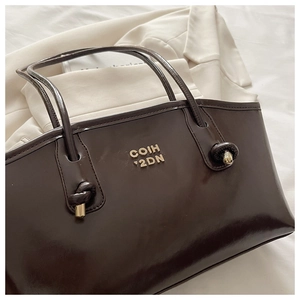 Close-up of chocolate brown patent leather tote bag with gold logo and knotted metal hardware
