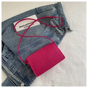 Detail of hot pink crocodile embossed baguette bag on blue denim and white fabric