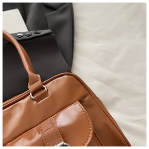 Detail of glossy brown leather tote showing fine stitching and metallic buckle accents