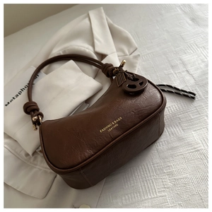 Detail of a brown leather crescent shoulder bag with knotted strap and gold lettering
