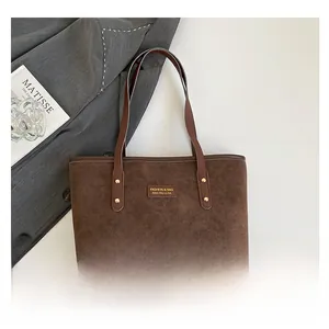 Detail of brown suede tote bag with leather handles and Fashion & Bag metal logo tag