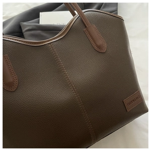 Detail of brown pebbled leather tote bag featuring a Fashion & Bags woven brand patch