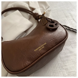 Close-up of brown leather crescent hobo bag with gold text and creative abacus pendant