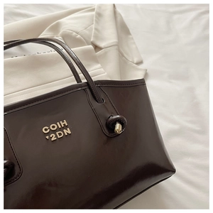 Detail of dark brown polished leather tote bag with elegant gold metal lettering