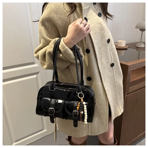 Detail of black patent leather shoulder bag with dual front pockets and beaded charm