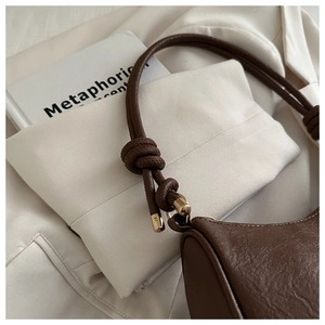 Detail of dark brown leather handbag featuring knotted shoulder strap and gold hardware