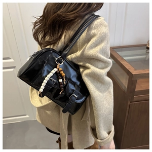 Detail view of black glossy shoulder bag with dual pockets and beaded charm on a model