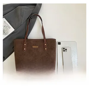Detail of dark brown suede tote bag with logo patch and reinforced metal rivets