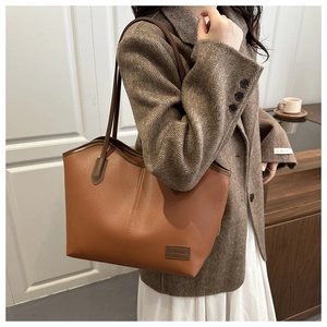 Detail of dark brown lychee grain leather tote bag with long shoulder straps and logo patch
