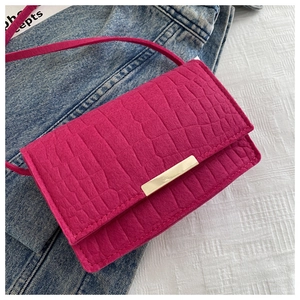 Detail of magenta faux leather bag with crocodile texture and gold metal buckle on denim