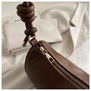 Close-up of brown leather bag with golden zipper and knot strap detail design
