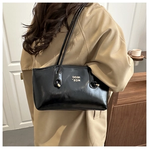 Polished black tote bag with slim straps and gold lettering on a beige trench coat
