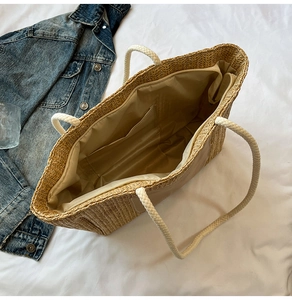 Detail view of woven straw tote bag featuring internal zip pocket and cotton rope handles