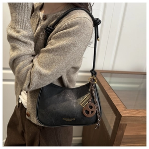 Detail of black leather half-moon shoulder bag with knot strap and golden charms