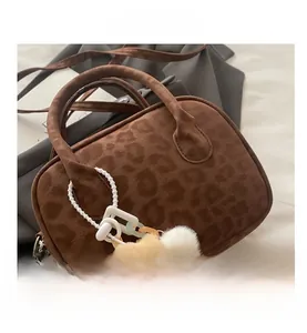 Detail of leopard print faux suede handbag featuring dual handles and plush bear charm