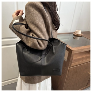 Detail of black lychee grain leather tote bag with fashion label and slim shoulder straps
