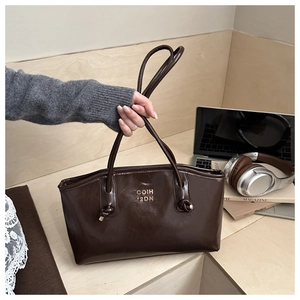 Brown leather tote bag with logo on wooden steps next to a laptop and headphones