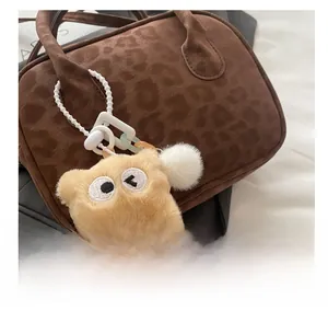 Close-up of yellow plush monster charm with beads on a leopard print handbag