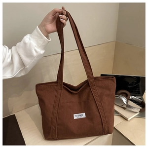Detail of a brown corduroy tote bag featuring a stitched white fashion label on fabric