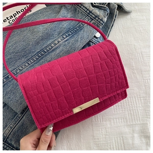 Macro detail of magenta faux suede crossbody bag with embossed crocodile texture and gold buckle