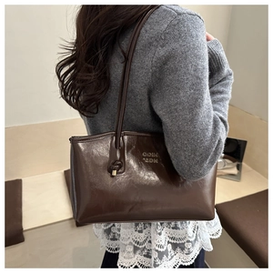 Detail of dark brown glossy leather tote featuring COIH '2DN embossing and knotted metal strap