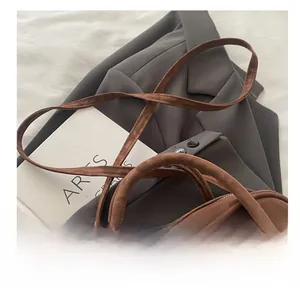 Detail view of brown suede shoulder bag with slim straps on gray blazer background
