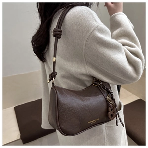 Detail view of dark brown leather shoulder bag featuring a unique metal abacus pendant