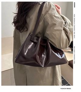 Detailed view of the dark brown glossy leather tote bag on a model wearing a trench coat