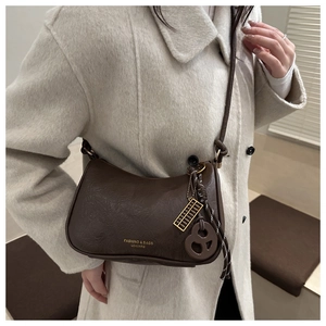 Detail of dark brown leather crescent bag with gold abacus pendant on beige wool coat
