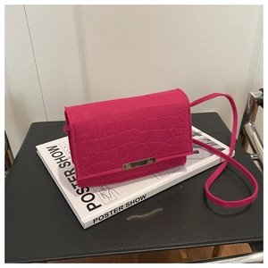 Detail of hot pink crocodile embossed crossbody bag with gold metal clasp on a magazine