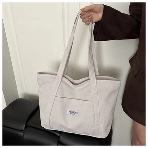 Close-up of off-white corduroy tote bag with Fashion Instinct patch and long shoulder strap