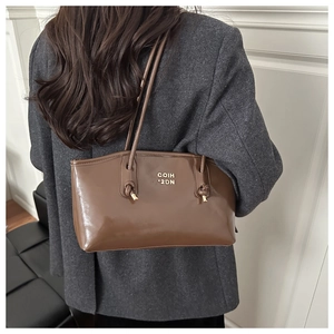 Detail of a brown glossy tote bag with a gold logo and slim shoulder strap
