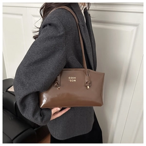 Detail view of brown glossy leather shoulder bag with gold lettering and side knot accents