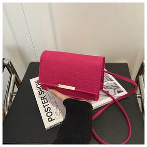 Detail of rose red square bag featuring crocodile embossing and gold metal fastener