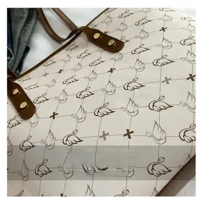 Detail of lychee textured tote bag with swan print and gold rivets on dark brown straps