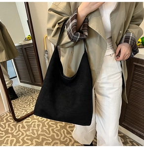 Close-up of minimalist black matte suede tote bag worn on shoulder in a home setting